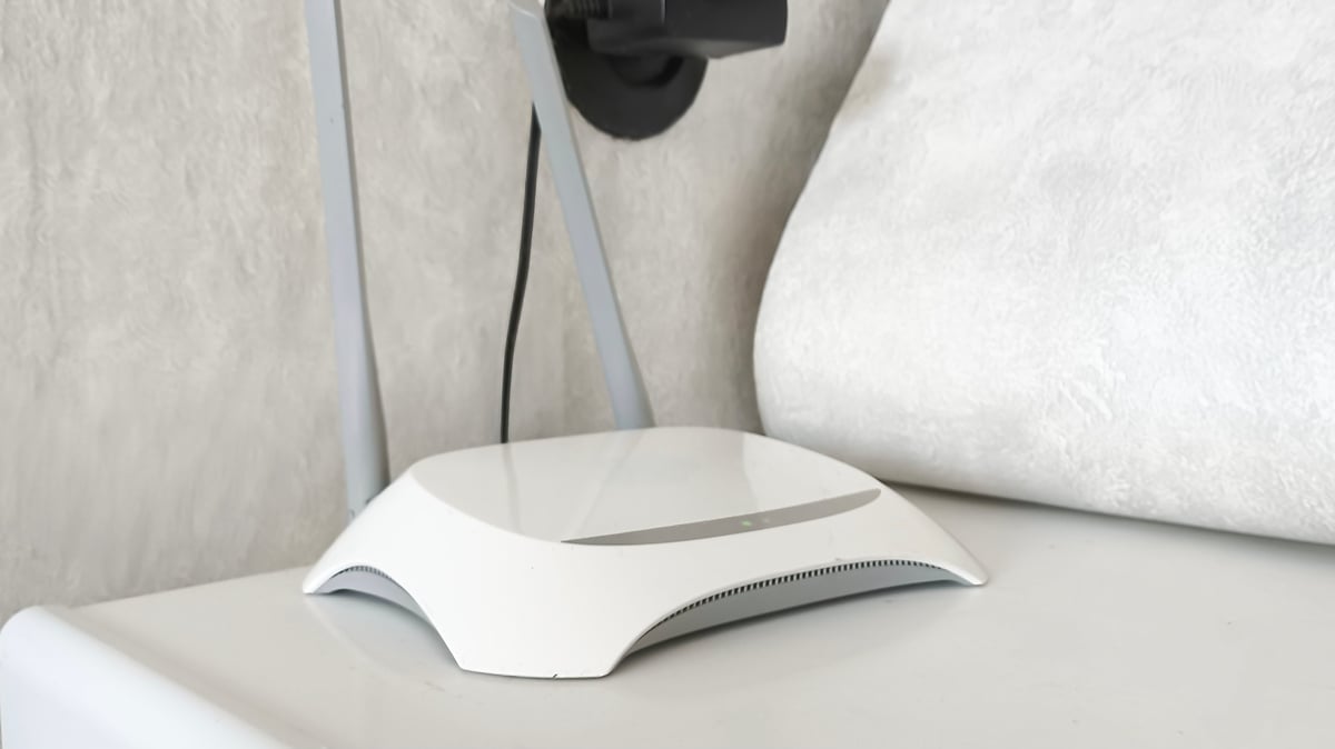 New white Wi-Fi router near potted plant on black shelf