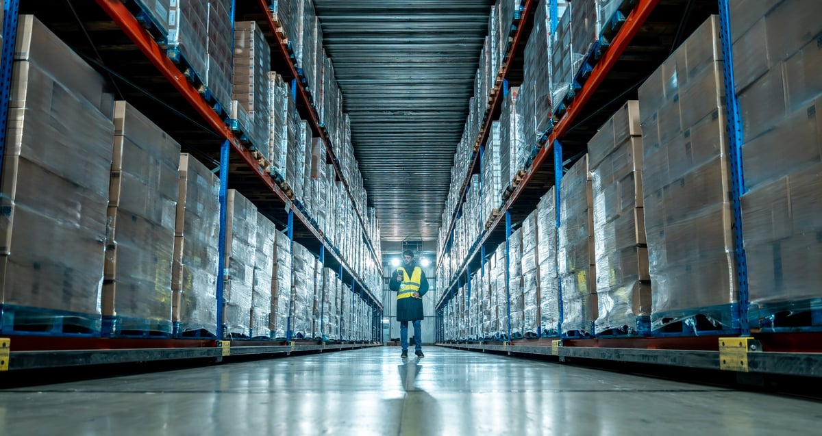 Worker in a high-visibility vest checking inventory in a large warehouse aisle