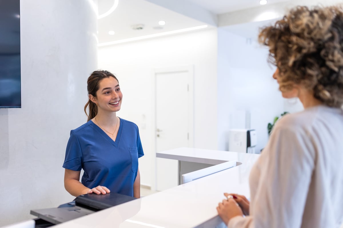 Friendly medical receptionist welcoming a patient at a modern clinic reception desk