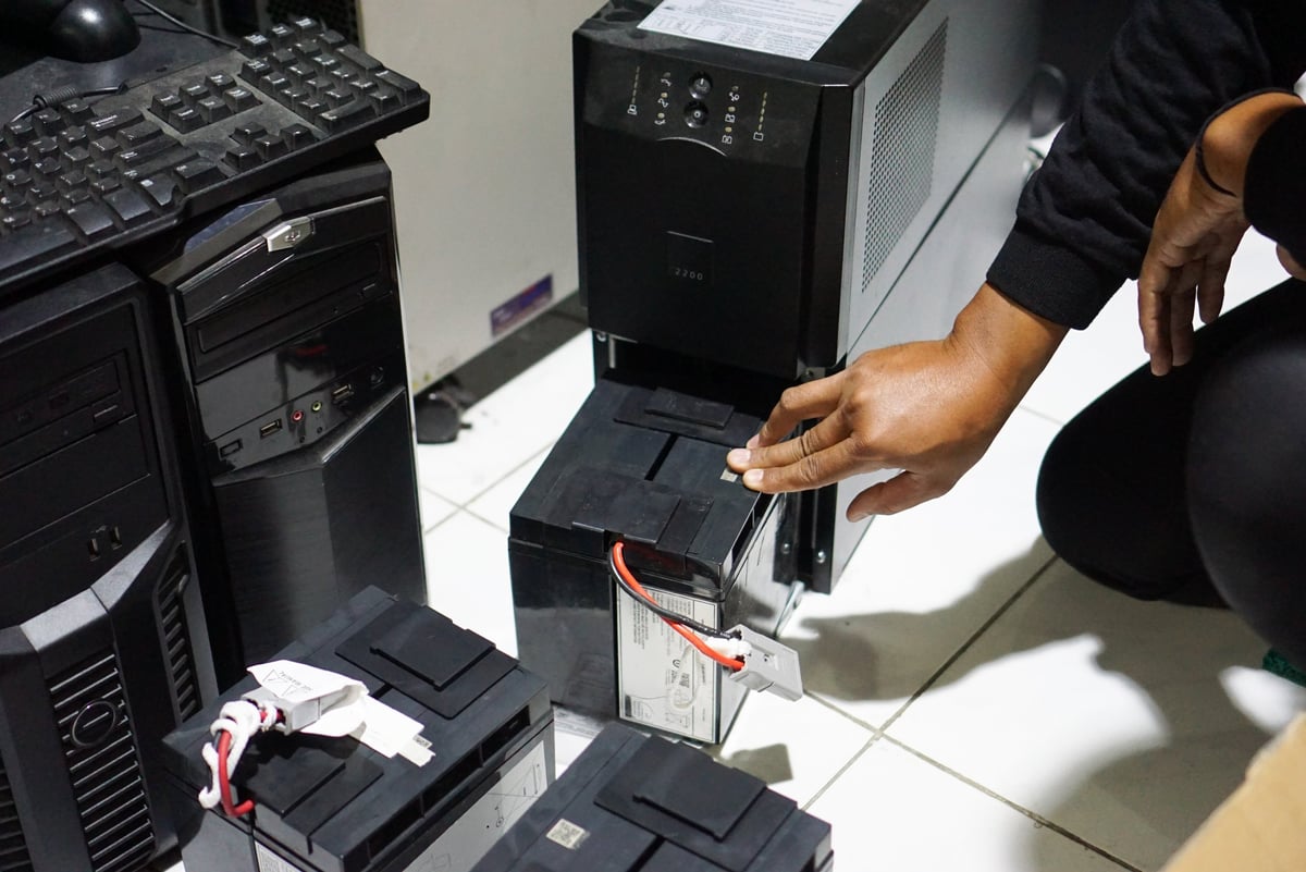 A man installing a replacement battery pack for an uninterruptible power supply, or UPS unit.